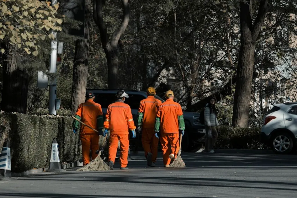 Quatro Trabalhadores De Saneamento Em Uniformes Laranja Com Vassouras ReaW3g8g9R0